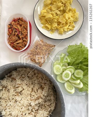 Nasi liwet made with fragrant rice cooked in coconut milk and spices, served with side dishes like chicken, tempeh, vegetables, and sambal, creating a rich and flavorful traditional Indonesian meal 135202207