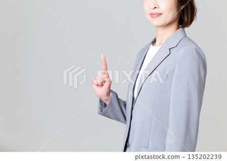 A middle-aged female business woman in a gray suit pointing up A middle-aged female business woman in a gray suit pointing up 135202239