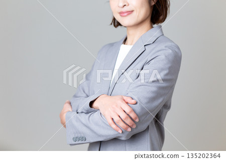 一位身穿灰色套裝、雙臂交叉抱在胸前的中年女商人 一位身穿灰色套裝、雙臂交叉抱在胸前的中年女商人 135202364