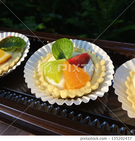A delightful fruit tart with a buttery, flaky crust filled with creamy custard and topped with an array of fresh, vibrant fruits. Perfectly balanced between sweet and tangy, making it irresistible 135202437