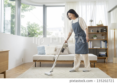 A woman in her 50s vacuuming in the living room 135202721