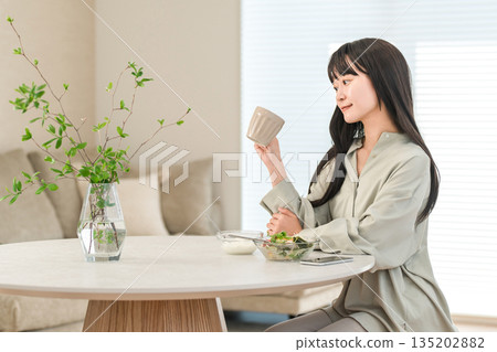 Young Asian woman drinking a hot drink at the dining table (warming up) Young Asian woman drinking a hot drink at the dining table (warming up) 135202882