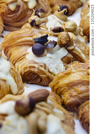 Group of fresh baked croissants, with topping of butter cream, caramel and roasted hazelnuts 135204025