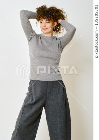 A woman stands with her hands behind her head wearing comfortable grey outfit A woman stands with her hands behind her head wearing comfortable grey outfit 135205303