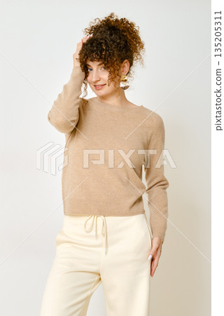 Model wearing a light brown sweater and cream pants posing against a plain background 135205311