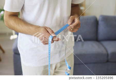 Hands of man holding measuring tape to measure waist, tracking body weight 135205896