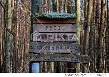 Warsaw, Poland, January 7, 2026 During the day, aged wooden signs with moss point the way through a serene forest. Directions include Park Kultury and Centrum Edukacji Przyrodniczo-Lesnej 135206762