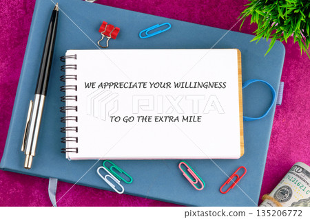 A notebook displays We Appreciate Your Willingness To Go The Extra Mile surrounded by office supplies. A blue journal, pen, and paperclips rest near rolled United States currency A notebook displays We Appreciate Your Willingness To Go The Extra Mile surrounded by office supplies. A blue journal, pen, and paperclips rest near rolled United States currency 135206772
