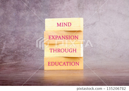 Four wooden blocks stacked say mind expansion through education. The blocks sit upon a table, in front of a gray and mottled backdrop promoting knowledge 135206782