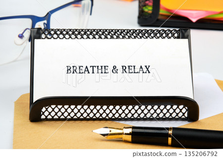 A calming message, BREATHE RELAX, is displayed on a white card in a black metal holder, resting on brown paper with a gold-nibbed fountain pen lying nearby 135206792