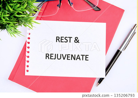 A note stating REST AND REJUVENATE is displayed on a red notebook surrounded by eyeglasses, a pen, and a small plant, encouraging relaxation and renewal A note stating REST AND REJUVENATE is displayed on a red notebook surrounded by eyeglasses, a pen, and a small plant, encouraging relaxation and renewal 135206793