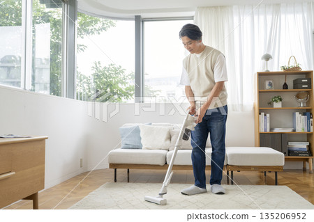 A man in his 50s vacuuming in his living room 135206952