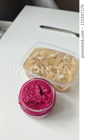 Beet spread in glass jar and plastic container on table as homemade food for lunch meal cuisine appetizer. Concept of simple meal preparation storage and comfort dining Beet spread in glass jar and plastic container on table as homemade food for lunch meal cuisine appetizer. Concept of simple meal preparation storage and comfort dining 135207179