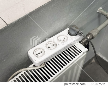 Power strip plugged into a radiator in a room corner. 135207594