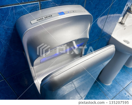 Automatic hand dryer on blue-tiled restroom wall. Automatic hand dryer on blue-tiled restroom wall. 135207595