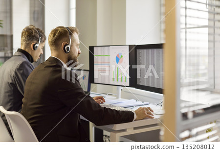 Call center analysts with headsets monitoring data on multiple computer screens Call center analysts with headsets monitoring data on multiple computer screens 135208012