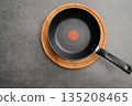 Minimalist presentation featuring skillet on textured surface with heat indicator, Stylish arrangement of nonstick pan on cork mat against textured grey background surface 135208465