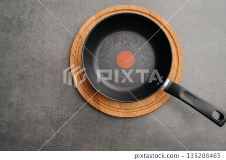 Minimalist presentation featuring skillet on textured surface with heat indicator, Stylish arrangement of nonstick pan on cork mat against textured grey background surface Minimalist presentation featuring skillet on textured surface with heat indicator, Stylish arrangement of nonstick pan on cork mat against textured grey background surface 135208465