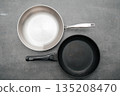 Stainless and black cookware overlapping on textured surface, Contemporary kitchen scene featuring overlapping pans with diverse finishes and subtle lighting effects 135208470