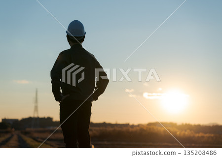 A man in work clothes standing with a sunset in the background 135208486