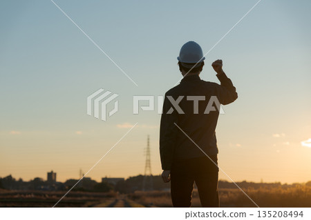 A man in work clothes standing with a sunset in the background 135208494