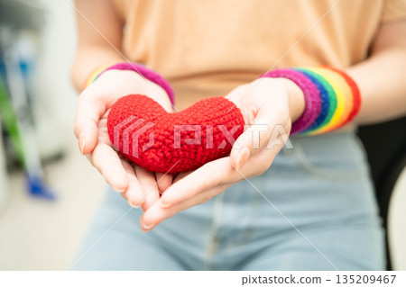 Asian woman holding LGBT heart with rainbow flag. Asian woman holding LGBT heart with rainbow flag. 135209467