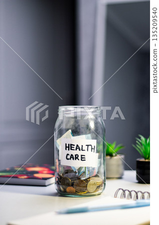 Health goal savings in labeled jar. Person contributing to Healthcare fund jar, representing wellness investment and proactive approach to medical expenses Health goal savings in labeled jar. Person contributing to Healthcare fund jar, representing wellness investment and proactive approach to medical expenses 135209540