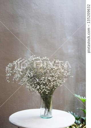 Beautiful dry grass flowers in glass vase decorated on white round table with vintage bare cement wall Beautiful dry grass flowers in glass vase decorated on white round table with vintage bare cement wall 135209632
