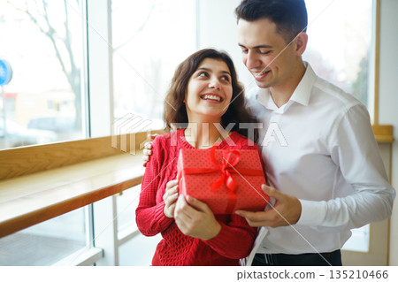 Man gives to his woman a gift box with red ribbon. A loving couple celebrating Valentine's Day. 135210466