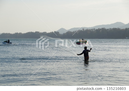 A man catches fish with a net in the sea, with a jet ski gliding in the background. A man catches fish with a net in the sea, with a jet ski gliding in the background. 135210803