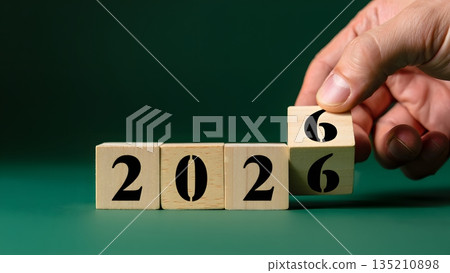 Hand Arranging Wooden Blocks to Display Year 2026 on Green Background 135210898