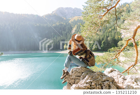 Young woman traveler enjoys fresh air and a beautiful view of the lake and mountains. Active life Young woman traveler enjoys fresh air and a beautiful view of the lake and mountains. Active life 135211210
