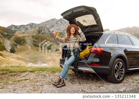 Young traveler woman taking a selfie by her car in the mountains during sunset. Lifestyle, travel Young traveler woman taking a selfie by her car in the mountains during sunset. Lifestyle, travel 135211348