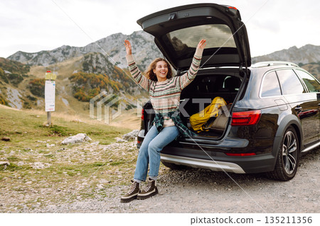 Young woman enjoying autumn nature while sitting in trunk of her car during a solo trip. Road trip Young woman enjoying autumn nature while sitting in trunk of her car during a solo trip. Road trip 135211356