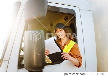 Portrait of beautiful young woman professional truck driver checking shipment list on a -parking lot Portrait of beautiful young woman professional truck driver checking shipment list on a -parking lot 135211488