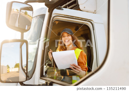 Portrait of beautiful young woman professional truck driver checking shipment list on a -parking lot Portrait of beautiful young woman professional truck driver checking shipment list on a -parking lot 135211490