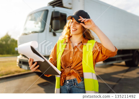 Portrait of beautiful young woman professional truck driver checking shipment list on a -parking lot 135211492
