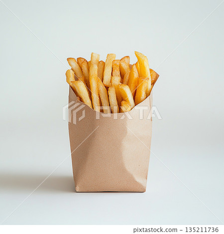 A brown paper bag filled with golden, crispy French fries is shown against a white background. A brown paper bag filled with golden, crispy French fries is shown against a white background. 135211736