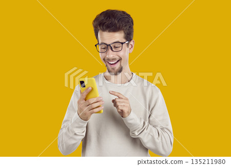 Happy smiling young man in glasses looking at message or notification on mobile phone Happy smiling young man in glasses looking at message or notification on mobile phone 135211980