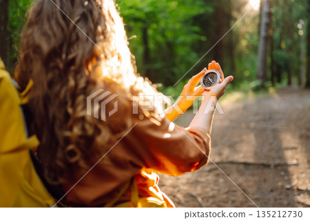 A hiker with curly hair holds a compass in their hands, carefully navigating through a sunlit forest A hiker with curly hair holds a compass in their hands, carefully navigating through a sunlit forest 135212730