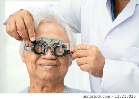 Optometrist checking Asian elderly woman ophthalmic vision eye test and using optical trial frame. Optometrist checking Asian elderly woman ophthalmic vision eye test and using optical trial frame. 135213026