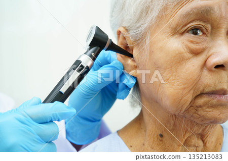 Otolaryngologist or ENT physician doctor examining senior patient ear with otoscope, hearing loss problem. Otolaryngologist or ENT physician doctor examining senior patient ear with otoscope, hearing loss problem. 135213083