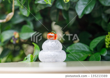 Glass Kagami mochi held up in a green garden Glass Kagami mochi held up in a green garden 135213389