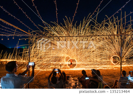 Tourists watch and record a spectacular fire spinning performance on the beach during a night event at Koh Samet, Rayong, Thailand 135213464