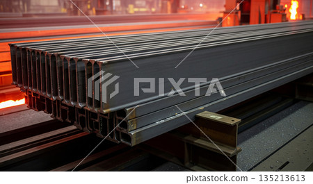 Steel I beams are stacked vertically in a manufacturing facility. The camera pans down the height of the stack, focusing on the arrangement of the beams in the space. 135213613