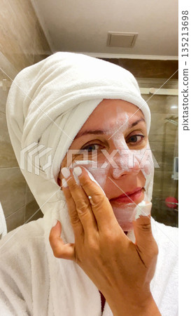 A young woman applies a nourishing care cream mask to her skin 135213698