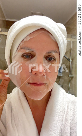 A woman straightens a cloth care mask on her face.  135213699
