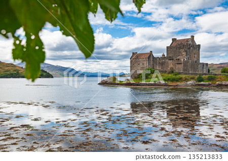 Eilean Donan Castle framed by leaves and calm water in Scottish Highlands 135213833