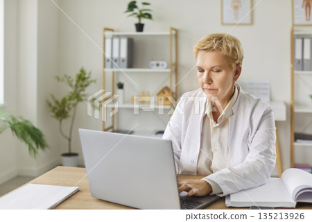 Mature doctor, focused attentive general practitioner in using laptop, giving online help, support Mature doctor, focused attentive general practitioner in using laptop, giving online help, support 135213926