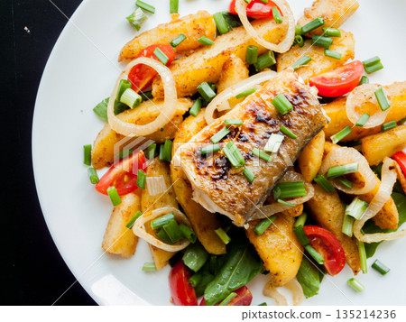 Plate with baked potatoes, piece of fish, vegetables and herbs on the table with tomato sauce. 135214236